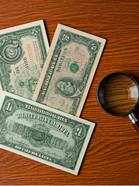 Billetes antiguos extendidos sobre una mesa de madera con lupa.
