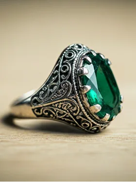 Anillo vintage con piedra verde y filigrana metálica sobre fondo neutro.